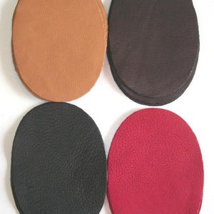 May include: Four leather patches in different colors: brown, black, black, and red. The patches are oval shaped and have a textured surface.
