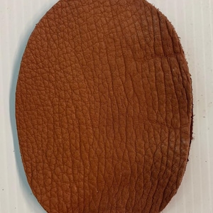 May include: A round piece of brown leather with a textured surface.