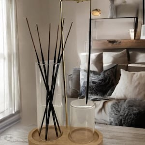 May include: A decorative aromatherapy diffuser set. The set includes a clear glass vase filled with black reeds, a small clear glass cup, and a gold-toned metal stand, all resting on a wooden tray. The diffuser is designed for home fragrance.