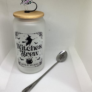 May include: A frosted glass tumbler with a bamboo lid, a black witch hat straw topper, and a long silver spoon. The tumbler has a black graphic that says "Witches Brew" with a witch flying on a broom and bats. The spoon has text.