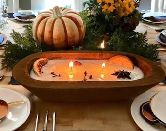 May include: A wooden dough bowl candle with two lit wicks, surrounded by dried orange slices, spices, and a pumpkin. The candle is set on a table with plates and silverware, creating a warm, inviting ambiance.