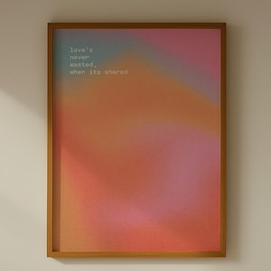 May include: A rectangular wall art print in a wooden frame featuring a blurred gradient of pink, orange, and red colors. The text "Love's never wasted, when its shared" is printed in small white letters in the upper left corner of the artwork.