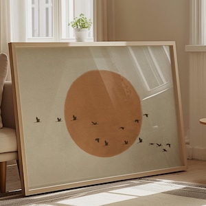 May include: A framed print with a minimalist design featuring a large orange circle and a flock of black birds flying in formation against a light grey background.