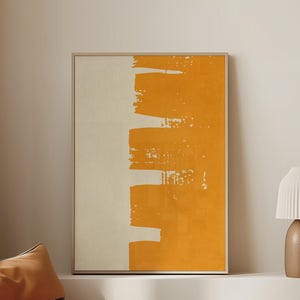 Può includere: Una stampa artistica astratta arancione e crema in una cornice dorata. Una moderna lampada da terra marrone con paralume plissettato è su una mensola bianca con libri. Un cuscino da pavimento marrone trapuntato è in primo piano.