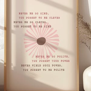 Może przedstawiać: Oprawiony wydruk z jasną drewnianą ramą. Wydruk ma beżowe tło z różowym wzorem kwiatowym i tekstem, który brzmi: „Never be so kind, you forget to be clever...“ Wydruk jest wyświetlany na białej powierzchni.