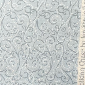 May include: Pale blue fabric featuring a repeating design of grey swirls and white dots. The fabric has a textured finish. The words "Holiday Cheer by Shade Forest" are printed vertically on the right edge.