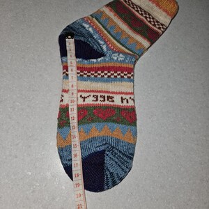 May include: A colorful patterned sock with a blue, red, white, and brown design. The sock is measured with a tape measure, showing a length of 19 inches.