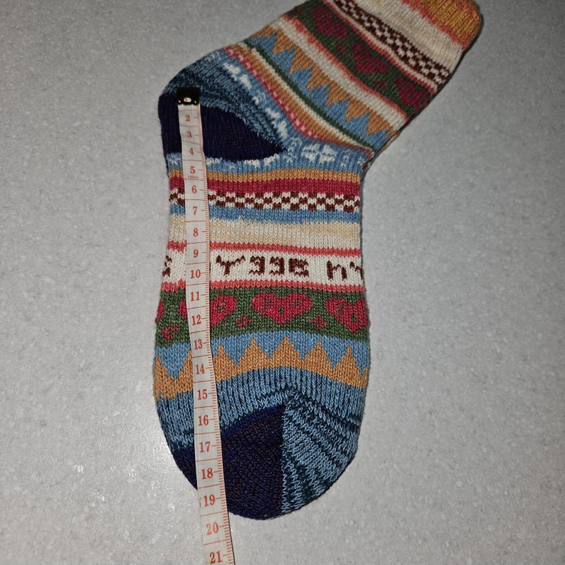 May include: A colorful patterned sock with a blue, red, white, and brown design. The sock is measured with a tape measure, showing a length of 19 inches.