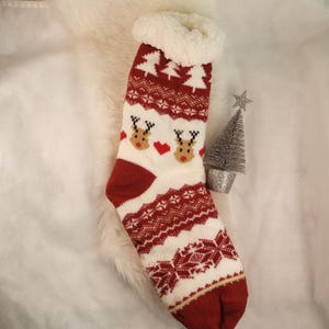 May include: Red and white Christmas-themed slipper socks with a reindeer pattern and a fluffy white cuff.