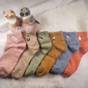 Könnte beinhalten: Sechs Paar Knöchelsocken mit gestickten Tiermotiven. Die Socken sind in verschiedenen Farben, darunter rosa, beige, grün, gelb, blau und orange.