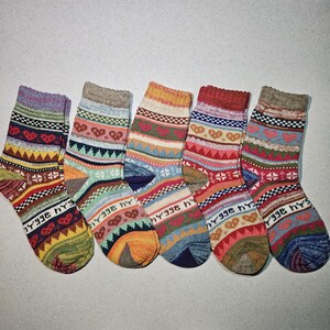 May include: Five pairs of colorful striped socks with a knitted pattern. The socks have a variety of colors including red, blue, green, yellow, and brown. The socks have a heart pattern and the word "hygge" written on them.