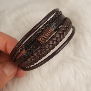 May include: A multi-layered brown leather bracelet with a braided design. The bracelet has a brown leather accent in the center.