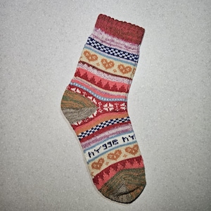 May include: A pair of colorful socks with a geometric pattern featuring hearts, stars, and stripes. The socks are made of a soft, knitted fabric and have a beige toe and heel.
