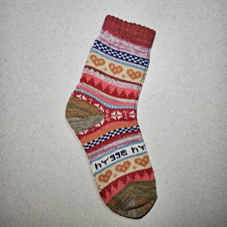 May include: A pair of colorful socks with a geometric pattern featuring hearts, stars, and stripes. The socks are made of a soft, knitted fabric and have a beige toe and heel.