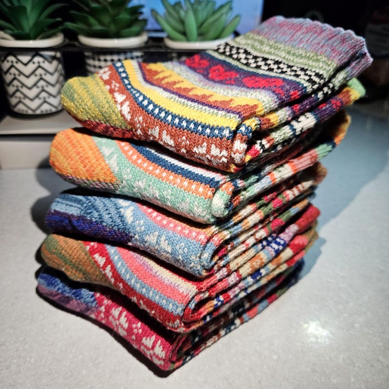 May include: A stack of colorful knitted socks with various patterns, including stripes, geometric designs, and snowflakes. The socks are made of a soft, warm material and are perfect for the winter season.