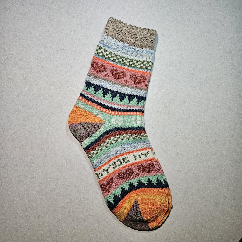 May include: A colorful patterned sock with a beige cuff. The sock has a geometric design with orange, blue, green, and brown accents.