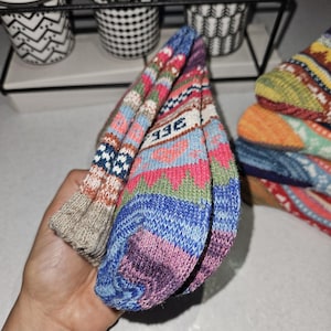 May include: A pair of colorful knitted socks with a geometric pattern. The socks are folded in half and have a beige, blue, pink, and green color scheme. The socks have the word "BEE" written on them.