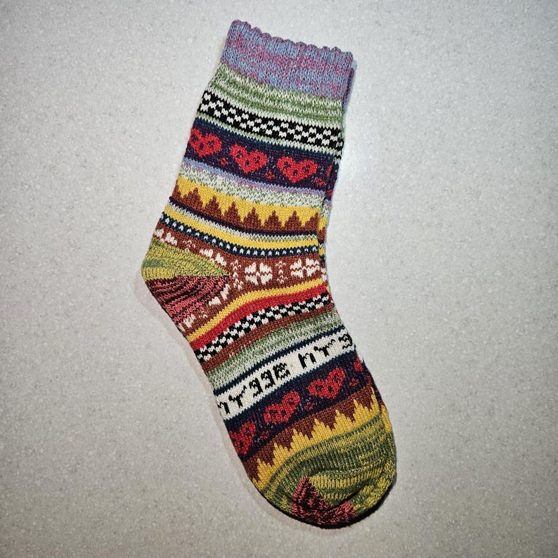 May include: A colorful striped sock with a pattern of hearts and geometric shapes. The sock is made of a soft, knitted fabric and has a light blue, green, yellow, red, brown, and black color scheme.