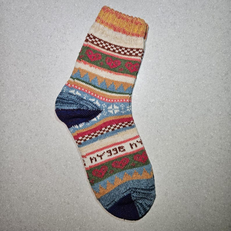 May include: A colorful patterned sock with a blue, red, yellow, and green design. The sock has the word "hygge" written on it.