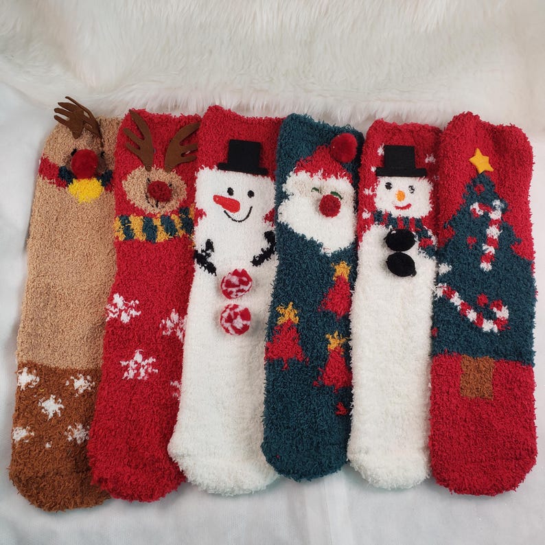 May include: Six pairs of fuzzy Christmas themed socks. The socks feature a reindeer, snowman, Santa Claus, a Christmas tree, and two snowmen. The socks are all in different colors, including red, green, white, and brown.