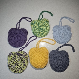 May include: Six handmade crochet soap savers in various colours: purple, green, yellow, blue, and dark grey. Each has a loop for hanging. The round, textured design is ideal for holding soap.