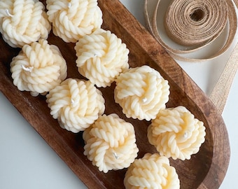May include: A wooden tray filled with eight white knotted candles. The candles are arranged in a circular pattern and are surrounded by a brown jute ribbon.