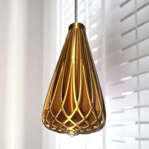 Könnte beinhalten: Eine goldfarbene Pendelleuchte mit geometrischem Design. Die Leuchte hat eine tropfenförmige Form mit vertikalen Rippen und einem dekorativen Rautenmuster am unteren Ende. Sie hängt an einem grauen Kabel.