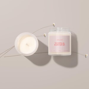 May include: A white candle in a glass jar with a pink label that reads "Smell & Love, Nesting & Baby Kicks".