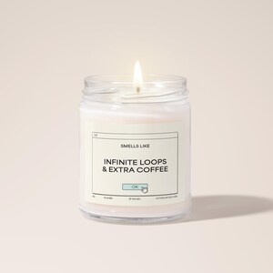 Puede incluir: Una vela blanca en un tarro de vidrio con una etiqueta que dice "Smells Like Infinite Loops & Extra Coffee". La etiqueta tiene un botón azul con la palabra "OK" y una flecha que apunta hacia él.