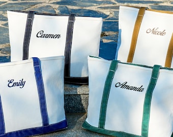 May include: Four white canvas tote bags with different colored accents and personalized names: "Carmen" with navy, "Nicole" with gold, "Emily" with blue, and "Amanda" with green. The bags are sitting on stone steps.