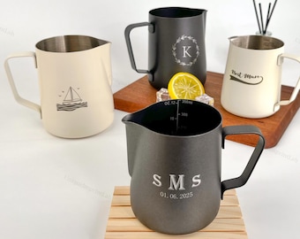 May include: Four stainless steel milk frothing pitchers in cream, black, and gray. One cream pitcher has a sailboat graphic, another has a letter "K", and a third has the text "Best Mom". The fourth pitcher has the initials "SMS" and the date "01.06.2025".
