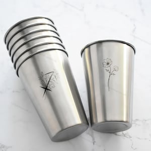 Op de afbeelding: Set van zeven roestvrijstalen bekers. De bekers hebben een zilveren afwerking en een zwart bloemmotief. De bekers zijn cilindrisch met een licht uitlopende bovenkant. Geschikt voor koude dranken.