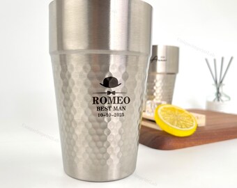 May include: A stainless steel tumbler with a textured surface and the text "ROMEO BEST MAN 10-10-2025" printed on the front. The tumbler has a hammered finish and a straight-sided design. A second tumbler is visible in the background.