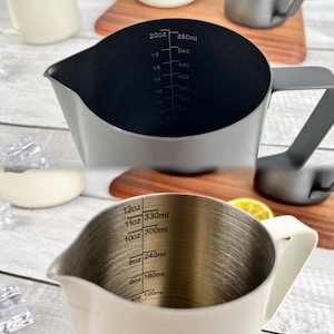 May include: Two stainless steel measuring pitchers with handles. One is dark gray with black interior markings for ounces and milliliters up to 20oz/580ml. The other is white with interior markings up to 12oz/330ml.