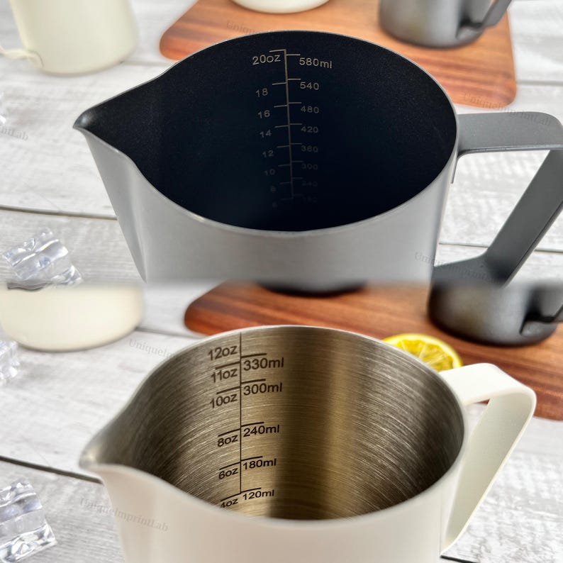 May include: Two stainless steel measuring pitchers with handles. One is dark gray with black interior markings for ounces and milliliters up to 20oz/580ml. The other is white with interior markings up to 12oz/330ml.