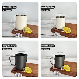May include: Four stainless steel milk frothing pitchers, two white and two black, with measurements in inches and ounces. Each pitcher is on a wooden board with a lemon slice and ice cubes.