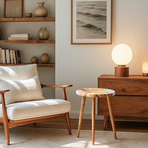 May include: A cozy living room scene featuring a wooden armchair with a white cushion and pillow, a small round side table, and a wooden cabinet. A globe lamp and a framed picture of ocean waves add to the room's ambiance.