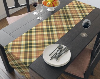 May include: A dining table set with a plaid table runner in shades of brown, green, and yellow. The table is set with plates, forks, wine glasses, and a bowl of apples. The table and chairs are dark wood.