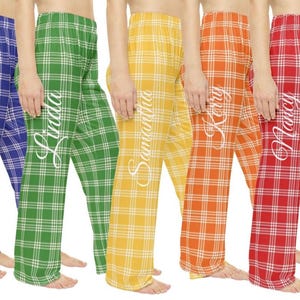 May include: Seven pairs of plaid pajama pants in purple, blue, green, yellow, orange, red, and pink. Each pair features a white grid pattern and a white cursive name printed vertically on the left leg: Alexis, Vaughn, Linda, Samantha, Kerry, Nancy, and Diana.