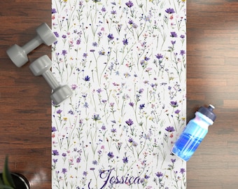 May include: A white yoga mat with a watercolor floral design in shades of purple, pink, and green. The mat has the name "Jessica" in a cursive font. Two gray dumbbells and a blue water bottle are next to the mat.