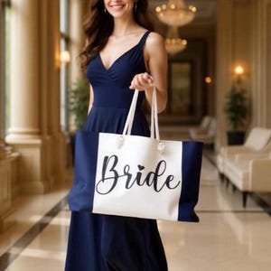 May include: A navy blue tote bag with the word "Bride" in elegant script. The bag has a white center panel and navy blue sides. The woman in the image is wearing a navy blue dress.