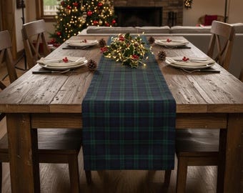 May include: A wooden dining table set for a holiday meal. A blue and green plaid table runner runs down the center, adorned with holly and lights. Plates, silverware, and pinecones are arranged for each place setting. A Christmas tree is visible in the background.