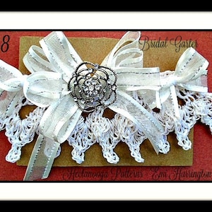 May include: White bridal garter with a white and silver bow and a rhinestone embellishment. The garter is on a brown background with the text "#1038 Bridal Garter Handmade Patterns Emma Harrington Designs".
