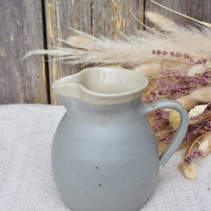 May include: A grey ceramic jug with a white rim and a speckled glaze. The jug has a rounded body and a handle.