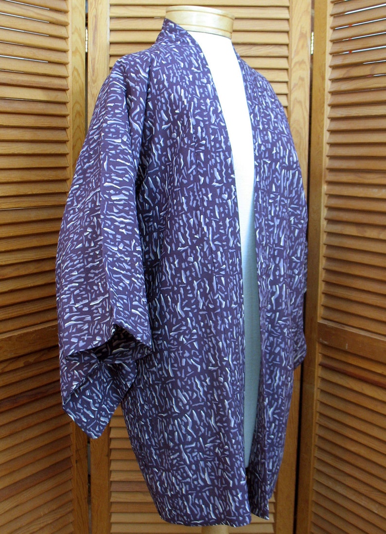 Puede incluir: Un kimono con estampado morado y blanco, con una abertura larga en la parte delantera y mangas anchas.