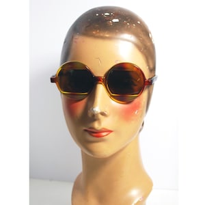 May include: A pair of round, tortoise shell sunglasses with brown lenses. The sunglasses are on a mannequin head.