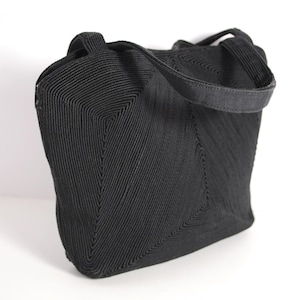 Könnte beinhalten: Eine schwarze gewebte Handtasche mit einem einzigen Henkel oben. Die Tasche hat ein geometrisches Muster und eine leicht abgerundete Form.