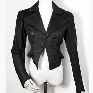 May include: A black cropped jacket with a double-breasted closure and five black buttons. The jacket has long sleeves and a pointed collar.