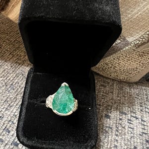 May include: A pear-shaped green gemstone ring set in silver. The ring is in a black velvet ring box.