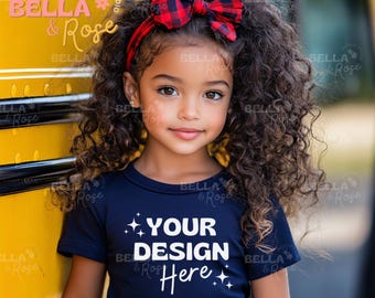 May include: A young girl with curly brown hair and a red plaid bow headband. She wears a navy blue t-shirt with the text "YOUR DESIGN Here" in white. The girl is also wearing a red plaid skirt.
